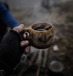 a person holding a cup in their hand with steam coming out of the top and leaves on it