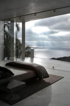 a bed sitting in the middle of a bedroom next to a large window with an ocean view