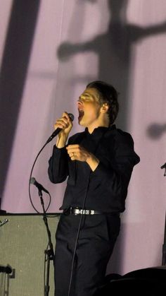 a man singing into a microphone while standing in front of a wall with shadows on it