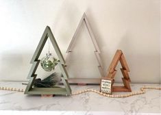 three wooden christmas trees sitting on top of a white counter next to a planter