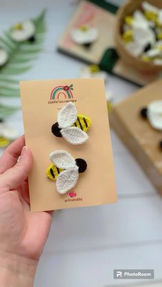 a person holding up two small crocheted bee pins on top of a piece of paper