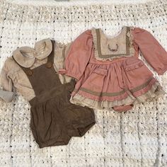 two baby clothes sitting on top of a white blanket