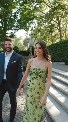 a man and woman holding hands while walking down some steps in front of trees with stairs leading up to them