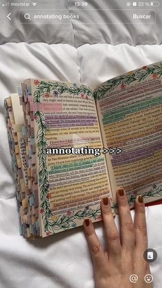 an open book sitting on top of a bed next to a person's hand