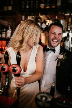 a man and woman standing next to each other in front of a bar filled with liquor bottles