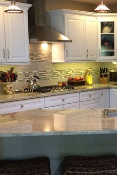 a kitchen with white cabinets and marble counter tops