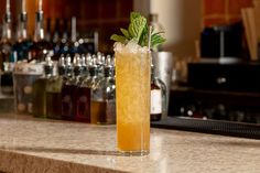 a tall glass filled with ice and mint sitting on top of a counter next to bottles