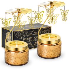 two gold candles in front of a box with butterflies on it and the candle is lit