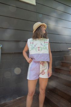 a woman standing in front of a house wearing shorts and a top with flowers on it