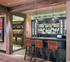 an image of a home bar with wine bottles on the wall and wooden stools