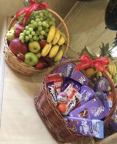 two baskets filled with fruit and chocolates on top of a wooden table next to a mirror