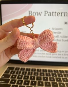 a hand holding a pink crocheted bow keychain in front of a laptop