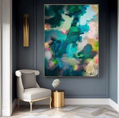 an abstract painting hangs on the wall next to a white chair and gold side table