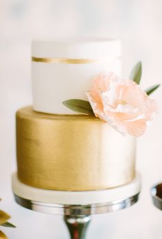 a white and gold wedding cake with a flower on top is sitting on a table