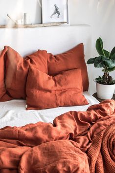 a bed with orange sheets and pillows on top of it next to a potted plant