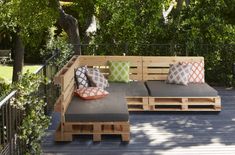 a couch made out of wooden pallets sitting on top of a deck next to trees