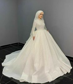 a woman in a white wedding dress standing next to a gray wall and black tile floor