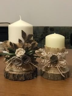 two white candles sitting on top of a wooden table next to each other and decorated with flowers