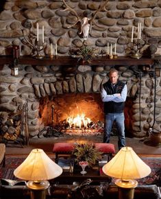 a man standing in front of a fire place with candles on the mantle and deer heads above it