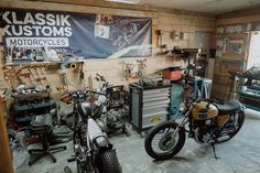 two motorcycles are parked in a garage next to other vehicles and tools on the wall