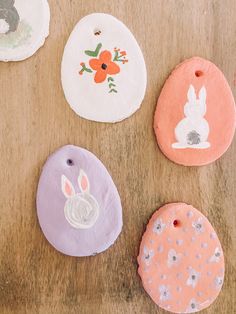 four handmade ornaments on a wooden surface with flowers and bunny faces painted on them