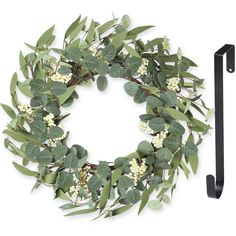 a wreath with white flowers and green leaves hanging on a black metal hook - up