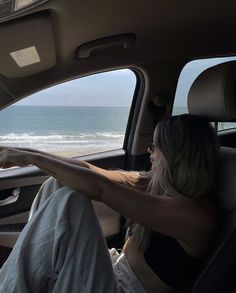 a woman sitting in the passenger seat of a car looking out at the ocean and beach