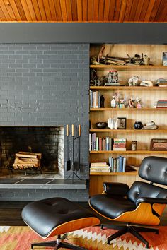 an eames chair and ottoman in front of a fireplace with bookshelves on either side