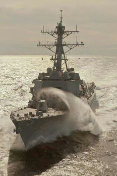 a navy ship in the ocean with water splashing up from it's hull