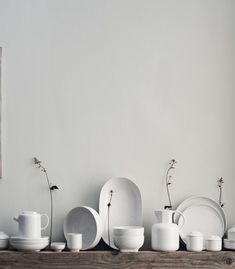 white dishes and vases are lined up on a shelf in front of a painting