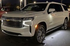 a white chevrolet suburban parked in a parking lot at night with other cars behind it