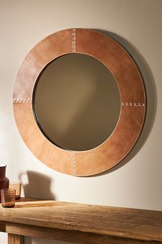 a round mirror sitting on top of a wooden table next to a vase and candle