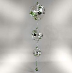 three glass balls are hanging from a metal rod with green leaves on it and one is upside down