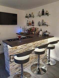 a bar with three stools in front of it and bottles on the wall behind it