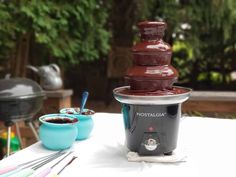 a chocolate fountain sitting on top of a table next to two bowls and spoons