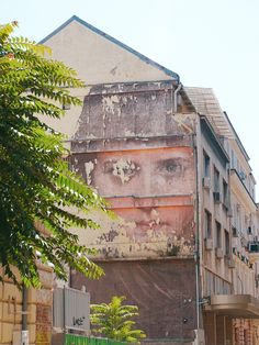 an old building with a face painted on it's side and trees in the foreground