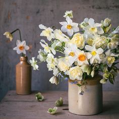 some white and yellow flowers are in a vase on a table with two brown vases