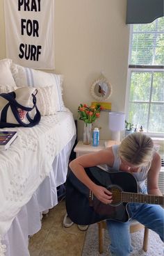 a woman sitting on the floor playing an acoustic guitar in front of a white bed