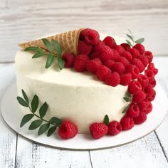 a white cake topped with raspberries and an ice cream cone on top of it