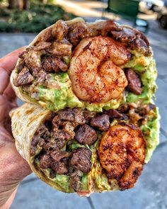 a person holding up a burrito with shrimp and guacamole on it