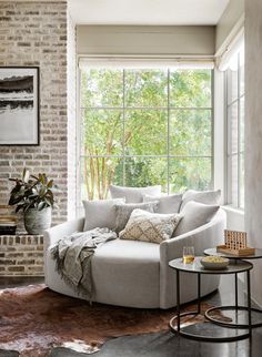 a living room filled with furniture next to a brick wall and window covered in windows