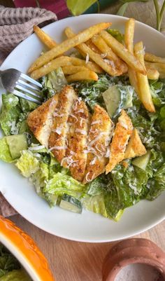 a white plate topped with lettuce and fish next to french fries on top of a wooden table