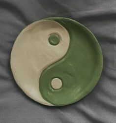 a green and white yin - yang dish sitting on a gray cloth covered tablecloth