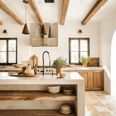 a kitchen with wooden beams and white counter tops, an island in the middle is surrounded by potted plants