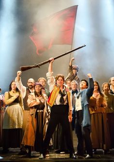 a group of people standing on top of a stage holding up a red and white flag