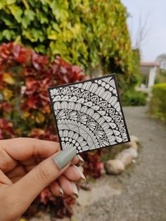 a person holding up a piece of paper with designs on it in front of some bushes