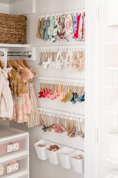 an organized closet with baby clothes hanging on the wall and other items in bins