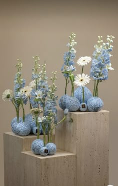 blue and white vases with flowers in them sitting on concrete blocks, against a beige background