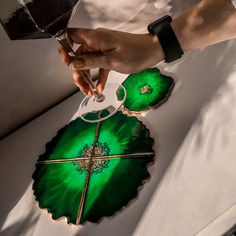 a person is holding a green leaf shaped tray with two rings on it and another piece of glass in the background