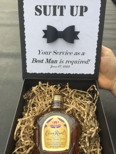 someone holding up a bottle of whiskey in a box that says suit up your service as a best man is required